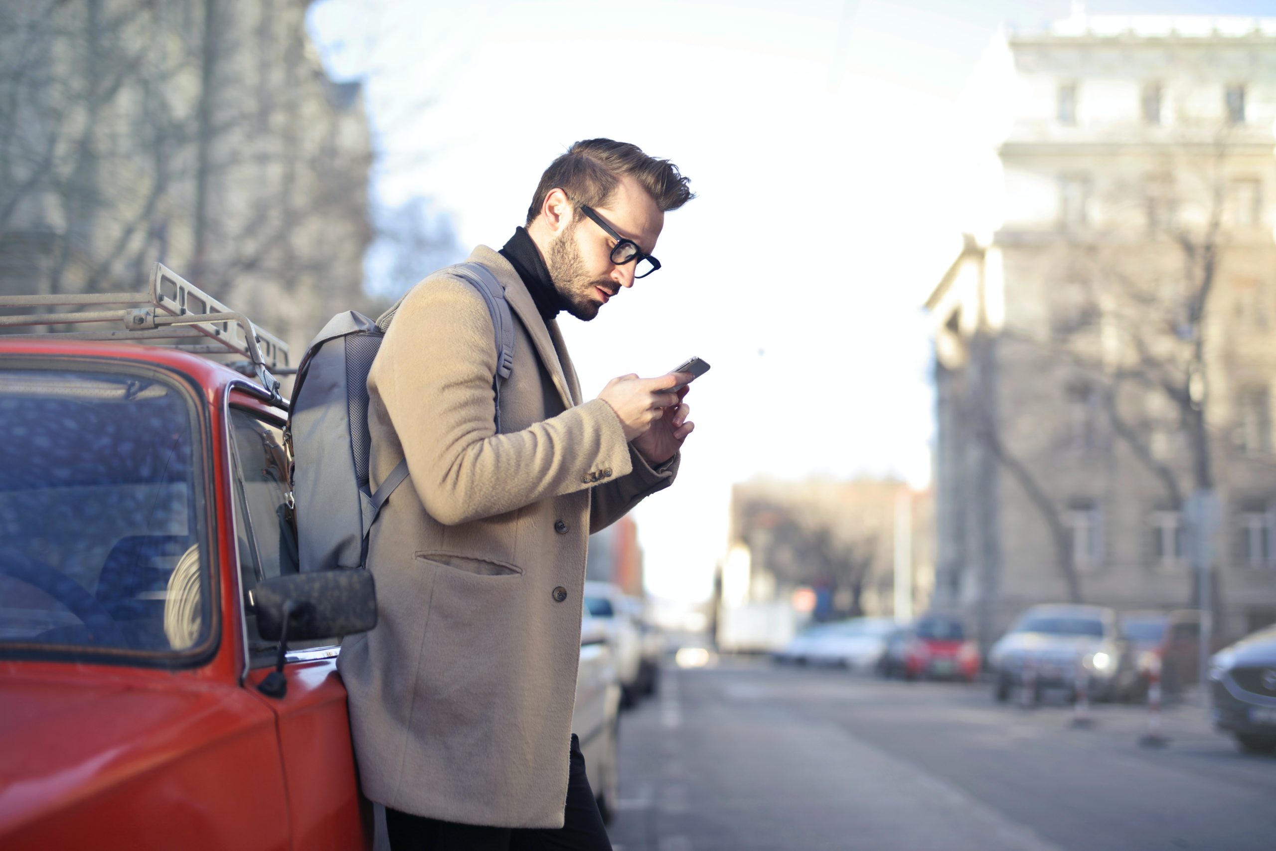 man using phone leaning against car